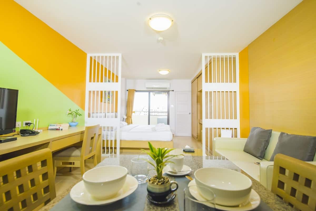 A hotel room with a bed, a desk with a computer, a dining table with bowls and a plant, and a sofa.