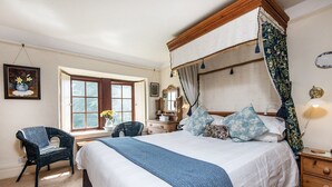Une chambre à coucher avec un lit à baldaquin, une fenêtre donnant sur un beau paysage, un fauteuil et une commode.