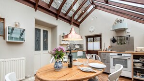 Une cuisine chaleureuse avec une table en bois, des chaises blanches et un porte-ustensiles suspendu au plafond.