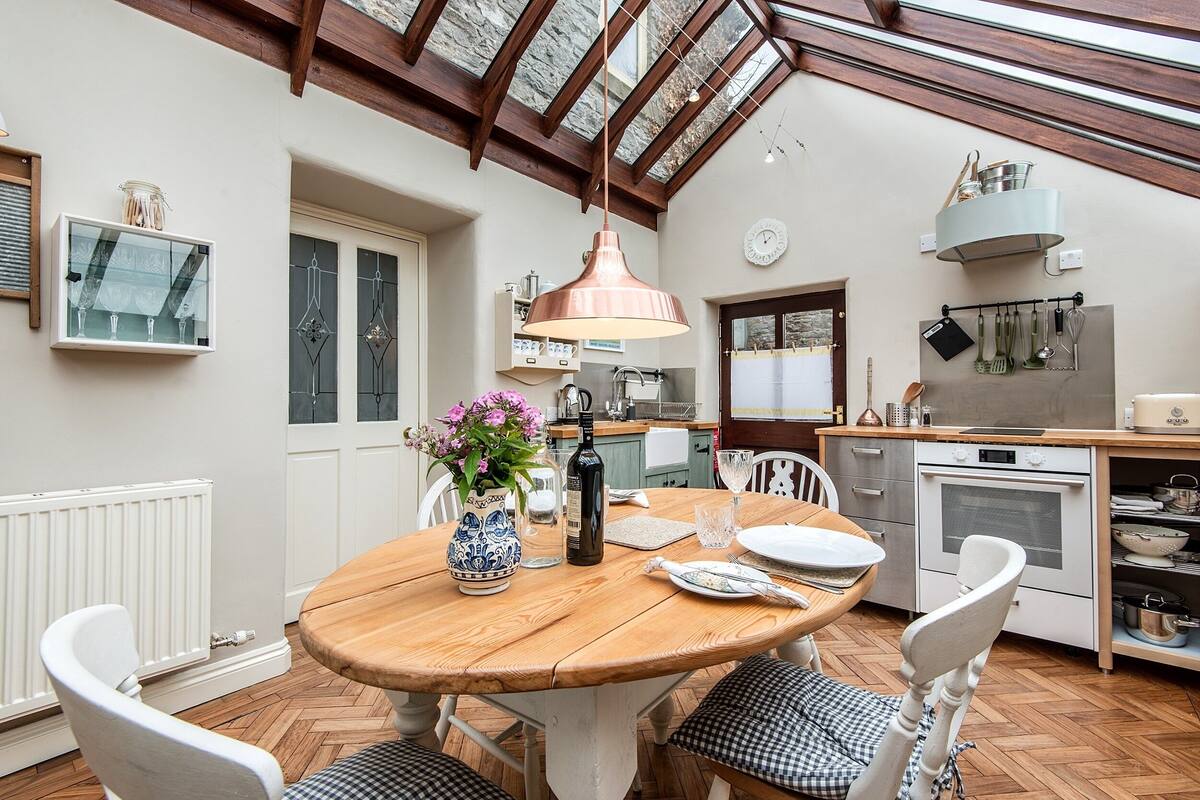 Una cocina acogedora con una mesa de madera, sillas blancas y un colgador para ollas.