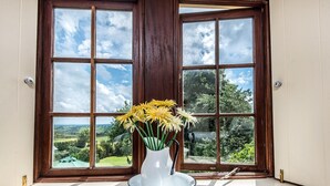 Un vase blanc orné de fleurs jaunes, posé sur une table ronde blanche près d’une fenêtre donnant sur un paysage verdoyant.