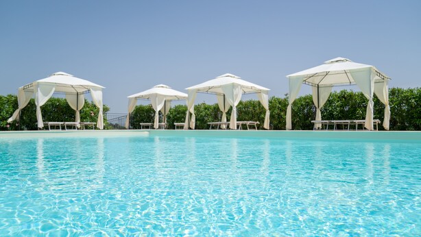 Une piscine à l’eau d’un bleu cristallin, surmontée de parasols blancs qui offrent de l’ombre.