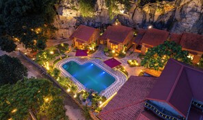 Ein Resort mit Pool, umgeben von Gebäuden mit roten Dächern, einem Steinweg und üppiger Vegetation.