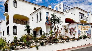 A white building with multiple arches and balconies, a mural on the side, and a clear blue sky.