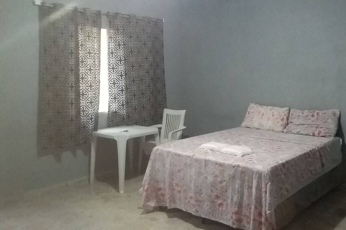 Un dormitorio con cama, una silla, una mesita y cortinas estampadas.
