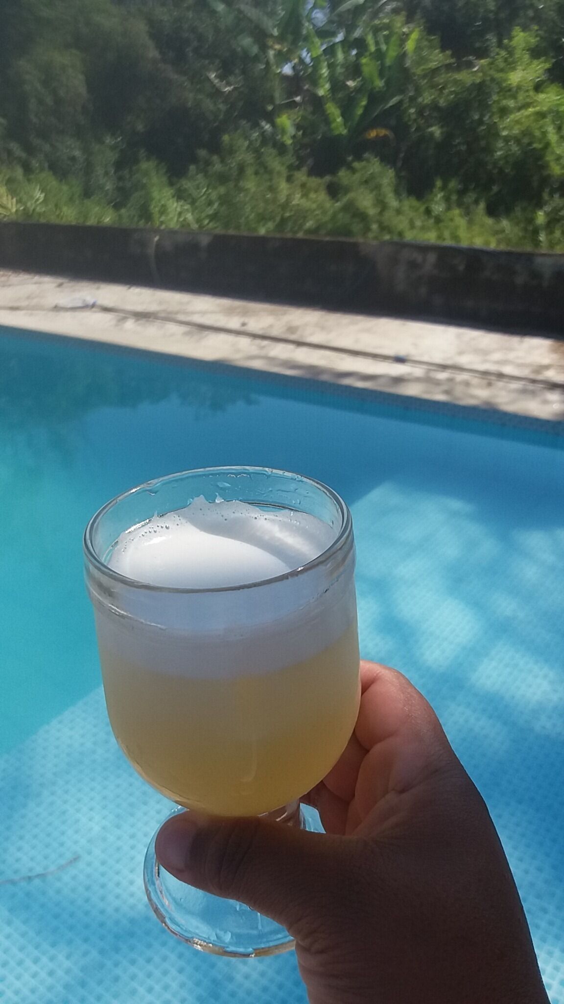 Una mano sosteniendo un vaso con una bebida en capas junto a una piscina.