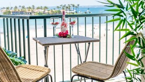 A balcony with wicker chairs, a small table with a bottle and flowers, and a view of the beach. - Luxury apartment Blue Sea in Alcudia beachview (Alcúdia)
