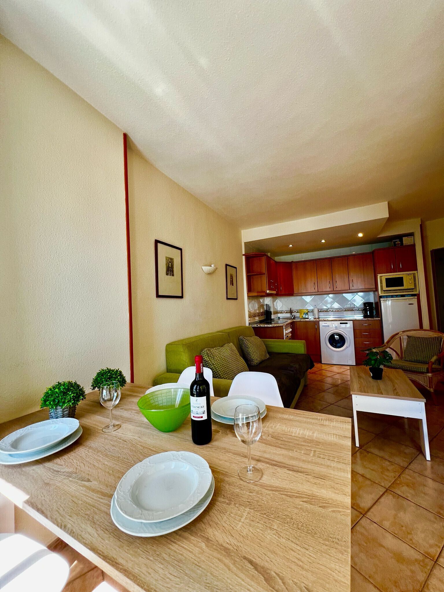 A dining area with a table set for two, a bottle of wine, and a green bowl.
