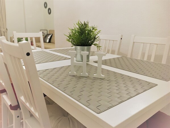 A dining table with white chairs, a potted plant, and a patterned table runner.