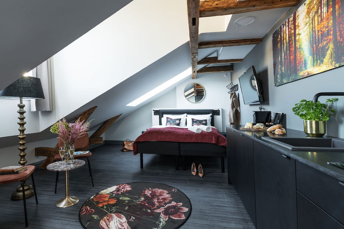 A modern bedroom with a sloped ceiling, a bed, a desk, and a large window.