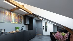 A modern kitchen with dark cabinetry, a wooden ceiling beam, and a large forest-themed artwork on the wall. - Hotel Filip (Oslo)