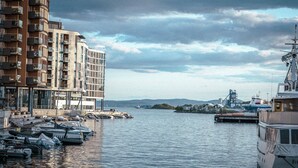 A marina with boats docked, a large building with balconies, and a distant view of hills. - Hotel Filip (Oslo)