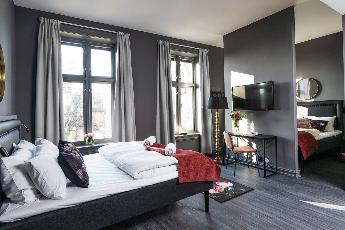 A modern hotel room with a large bed, a desk, a TV, and a view of the city.
