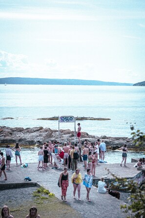 A crowded beach with a sign reading "OSLO" and rocky terrain. - Hotel Filip (Oslo)