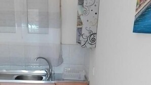 A small kitchen with a sink, a cabinet, and a dining table set with a placemat, two mugs, and a small bowl. - Anemologio Studios (Kefalonia)