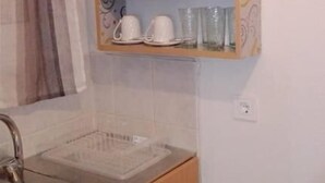 A kitchen with a wooden cabinet holding dishes, cups, and glasses. - Anemologio Studios (Kefalonia)