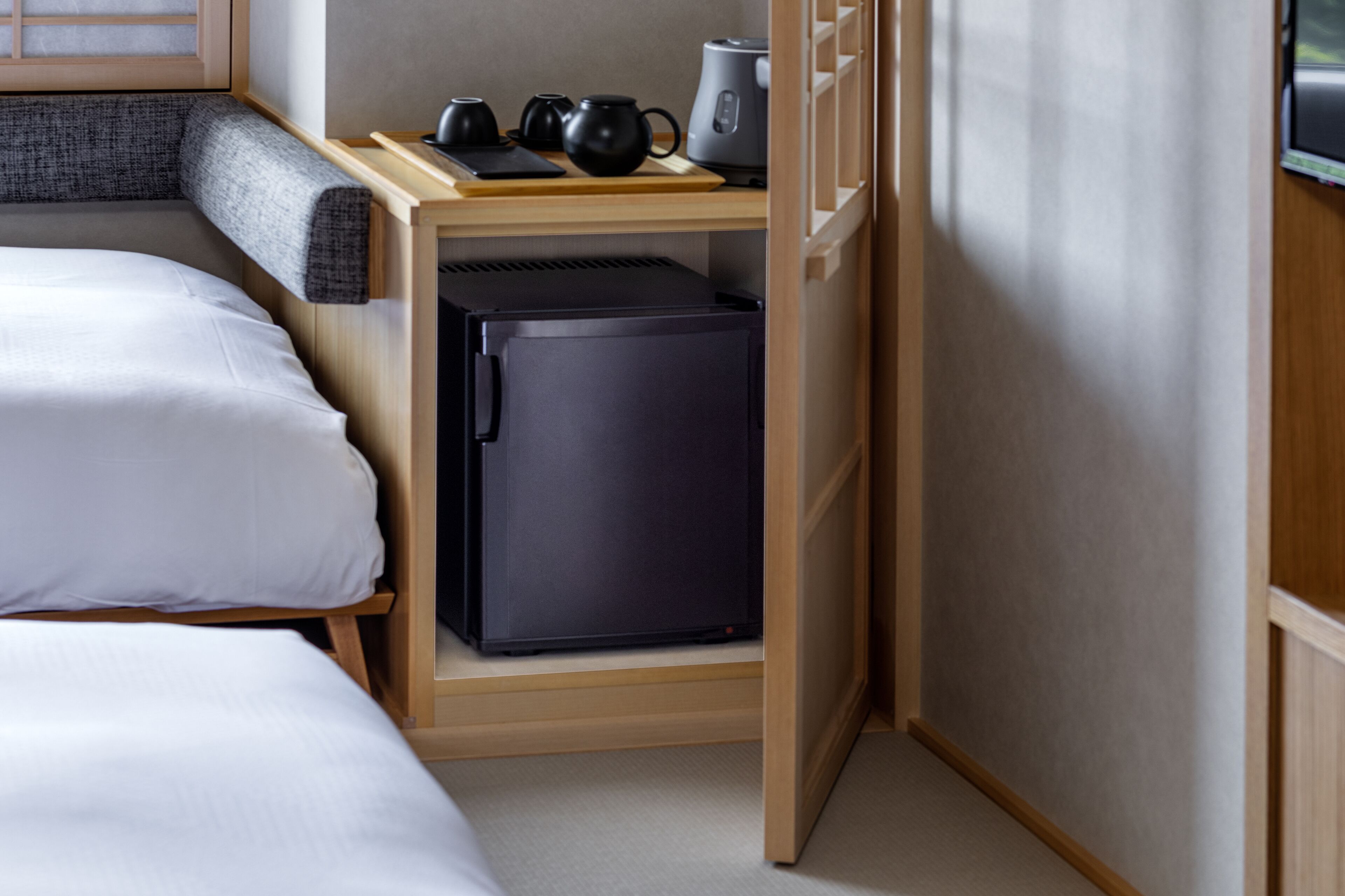 A compact hotel room with a bed, a small kitchenette with a refrigerator, and a wooden nightstand.