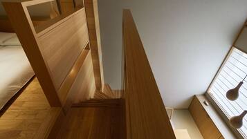 A compact, modern bedroom with a bunk bed, built-in shelving, and a sloped ceiling.