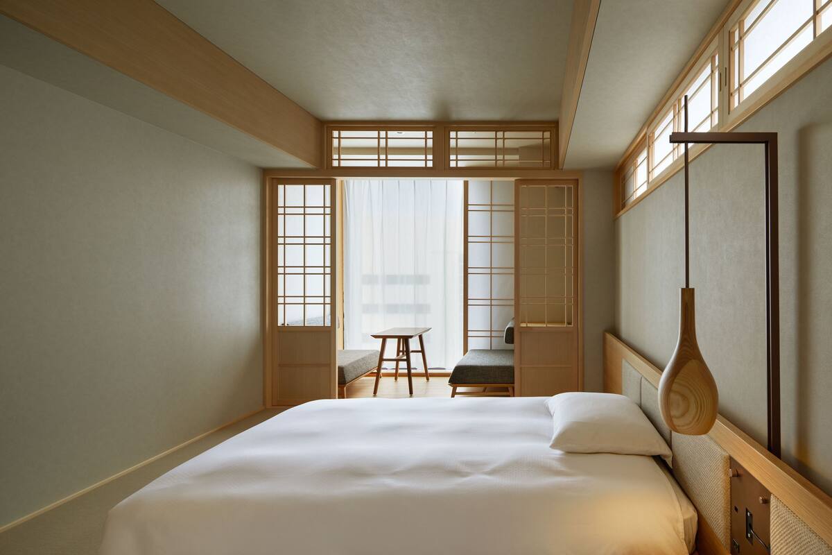 A hotel room with a large bed, a desk, and a chair. There is a window with a view of the outside.