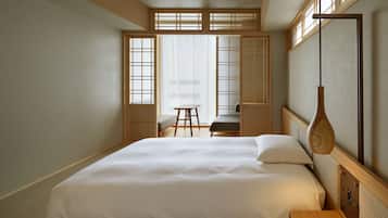 A hotel room with a large bed, a desk, and a chair. There is a window with a view of the outside.