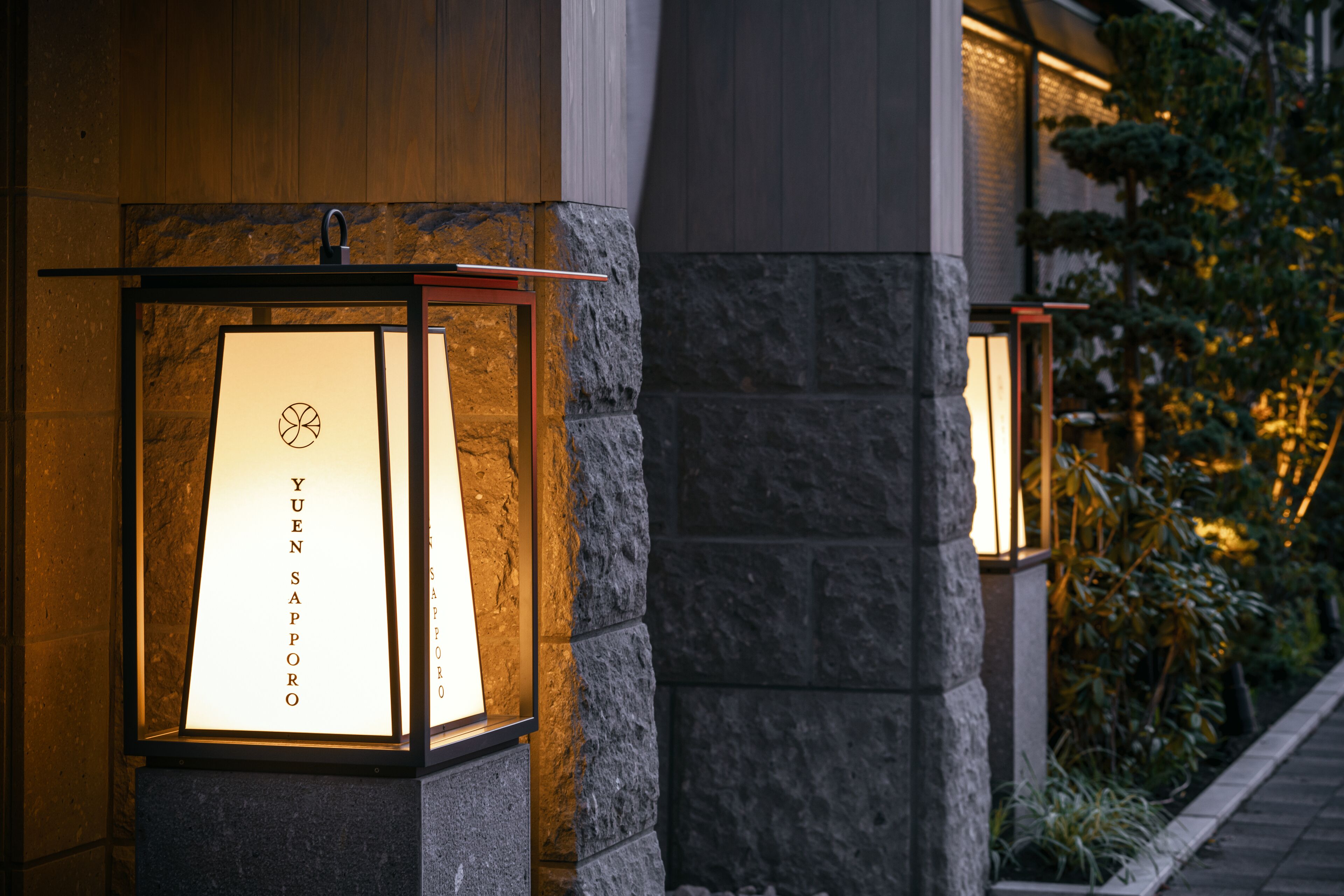 Two illuminated lanterns with the text "YUEN SAPPORO" mounted on stone pillars.