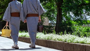 Two individuals in traditional attire walking on a pathway with a garden and a fence in the background.