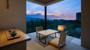 A modern room with a wooden table and chairs, a vase with branches, and a view of a cityscape at dusk. - Onsen Ryokan Yuen Sapporo (Sapporo)