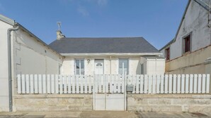 Un bâtiment blanc avec un toit gris, une clôture blanche faite de piquets et un portail fermé.