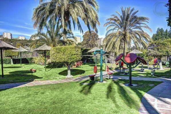 A well-maintained park with exercise equipment, palm trees, and a clear sky.
