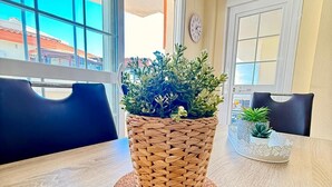 Een eettafel met een gevlochten mand met groene planten, twee stoelen en uitzicht door grote ramen.