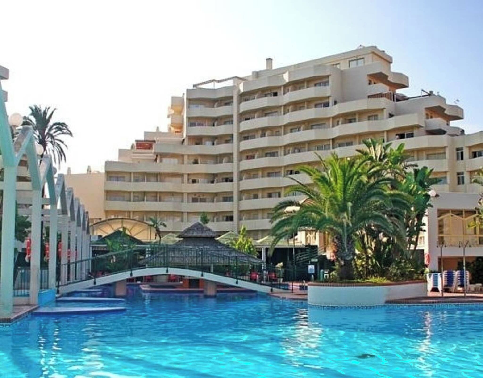 A hotel with a swimming pool, a bridge, and palm trees.
