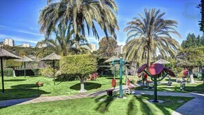 Un parque bien cuidado con equipo de ejercicio, palmeras y un cielo despejado.