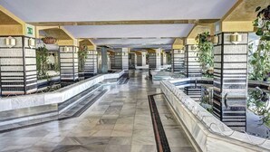 En modern hotellobby med en lång korridor, kaklade väggar och krukväxter.