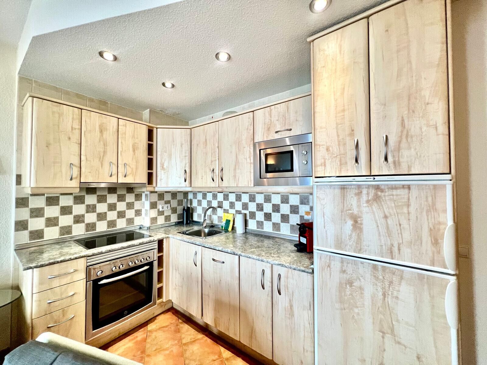 Una cocina compacta con armarios de madera, horno empotrado, microondas y fregadero.
