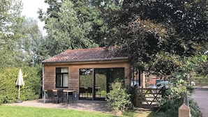 Une petite maison de plain-pied, avec un toit en tuiles, une terrasse avec une table et des chaises, et un jardin qui l’entoure.