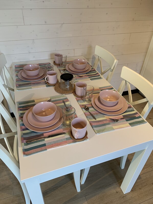 Une table à manger dressée avec des assiettes, des bols et des tasses roses, ainsi qu’un set de table à rayures.