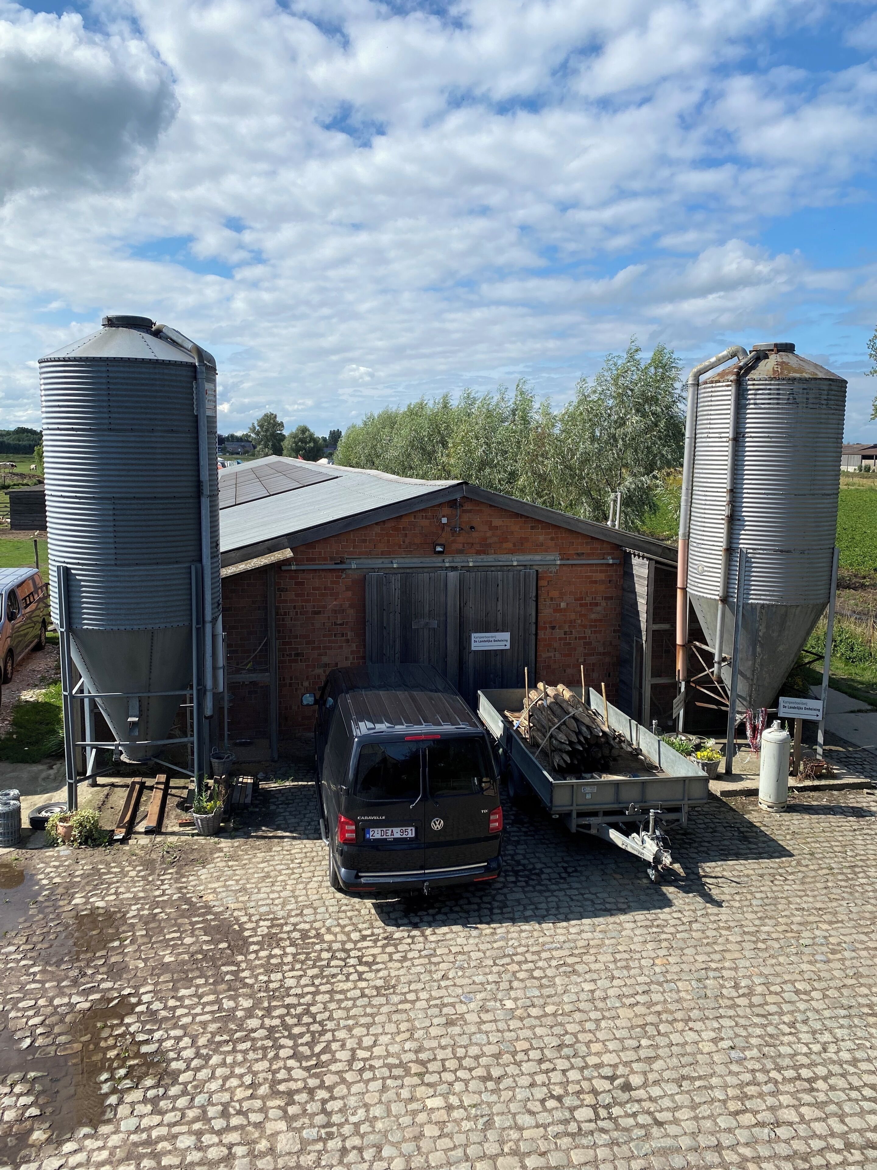 A building with two large cylindrical silos, a parked car, and a wooden pallet outside.