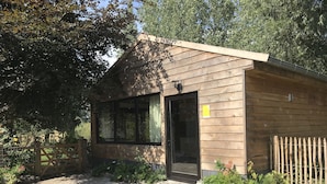 Une petite cabane en bois avec une porte noire, une fenêtre et un petit jardin agrémenté de plantes et d’un pot de fleurs.