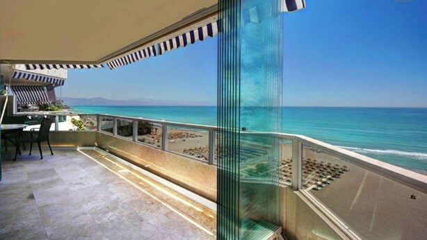 A balcony with a clear view of the ocean, a seating area, and a glass partition.