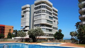 A modern building with a pool, surrounded by palm trees and a clear sky.