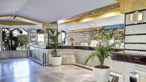 Un hall d’entrée avec un sol en marbre, des plantes en pot, un comptoir de réception et un mur recouvert de carreaux sur lequel est affiché un panneau indiquant « BLQ ».