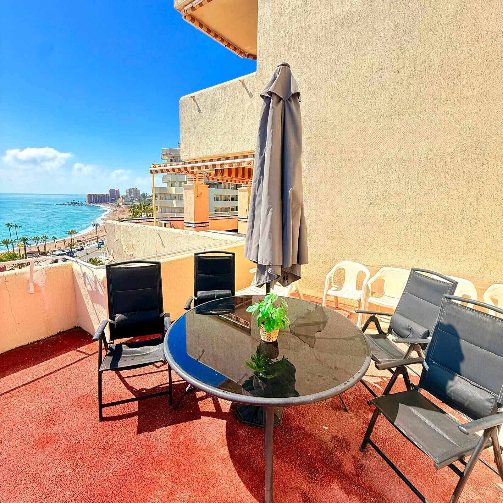 Ein runder Tisch mit Stühlen und einem Sonnenschirm auf einem Balkon mit Blick auf Strand und Stadtlandschaft.