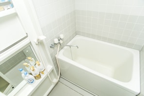 A bathroom with a white bathtub, a shower, and a shelf with toiletries. - Shinsaibashi-House A (Osaka)