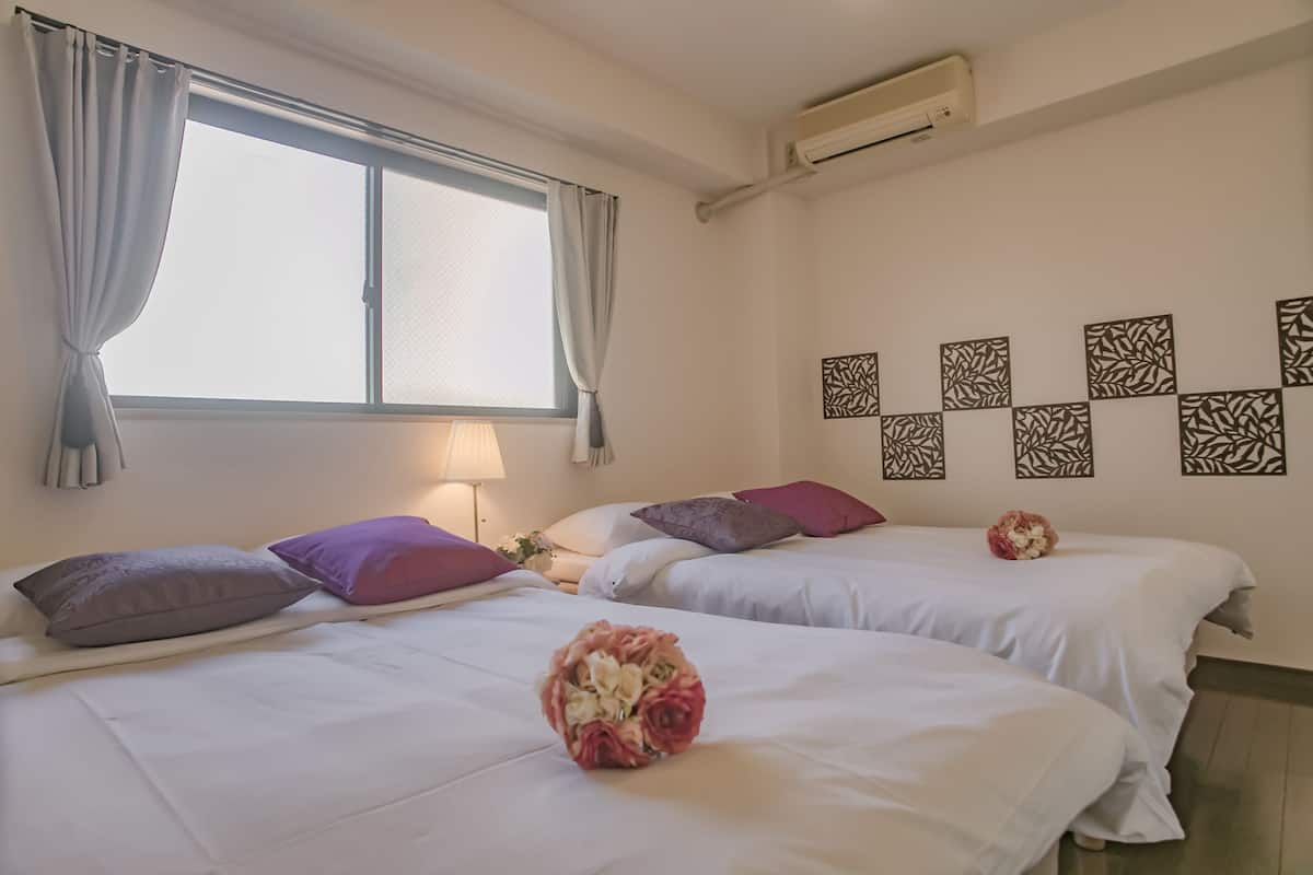 Quarto de hotel com duas camas, janela com cortinas, ar condicionado e arte decorativa na parede.