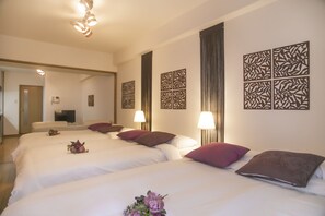 A hotel room with three beds, each with white linens and decorative pillows. There are wall-mounted lamps and a flat-screen TV on a stand. - Shinsaibashi-House B (Osaka)