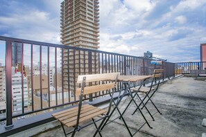 A rooftop terrace with a metal railing, wooden benches, and a view of high-rise buildings. - Shinsaibashi-House B (Osaka)