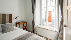 A bedroom with a bed, a bedside table with a lamp, a window with curtains, and a view of the outside. - Rodrigo Triana 1. 1 bedroom, shared terrace (Sevilla)