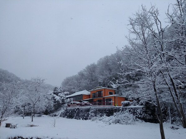 A two-story building with a red facade, surrounded by snow-covered trees and a hillside. - Akiu Canada (Sendai)
