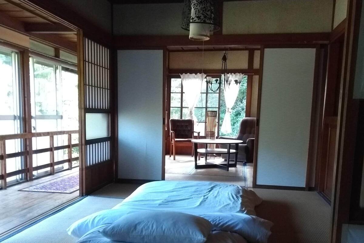 A traditional Japanese-style room with tatami flooring, a low wooden bed, and sliding doors leading to a balcony.