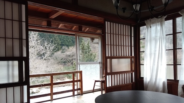 A traditional Japanese room with tatami flooring, a round table, and a view of a forested area through shoji screens. - Akiu Canada (Sendai)